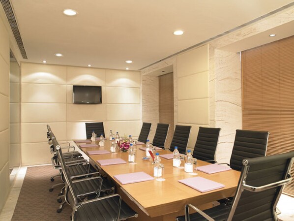 A conference room with a long table, black chairs, and a flat-screen TV on the wall. - Royal Orchid Central Grazia (Navi Mumbai)