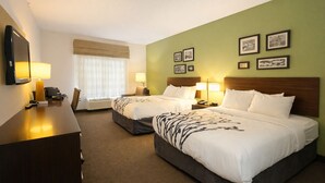 A hotel room with two beds, a desk, a chair, a TV, and framed pictures on the wall.