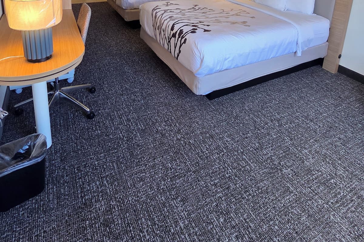 A hotel room with two beds, a desk with a lamp, and a small trash bin.