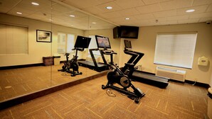 Une salle de sport équipée de matériel d’exercice, dotée d’un grand miroir et d’un téléviseur fixé au mur.