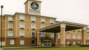 Un hôtel reconnaissable à son grand panneau indiquant « Express Inn & Suites », avec une entrée imposante dotée d’un espace abrité et arborant un drapeau américain.