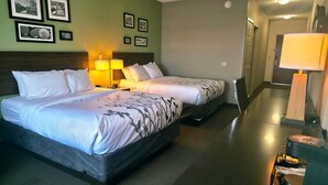 A hotel room with two beds, a nightstand with a lamp, and framed pictures on the wall.