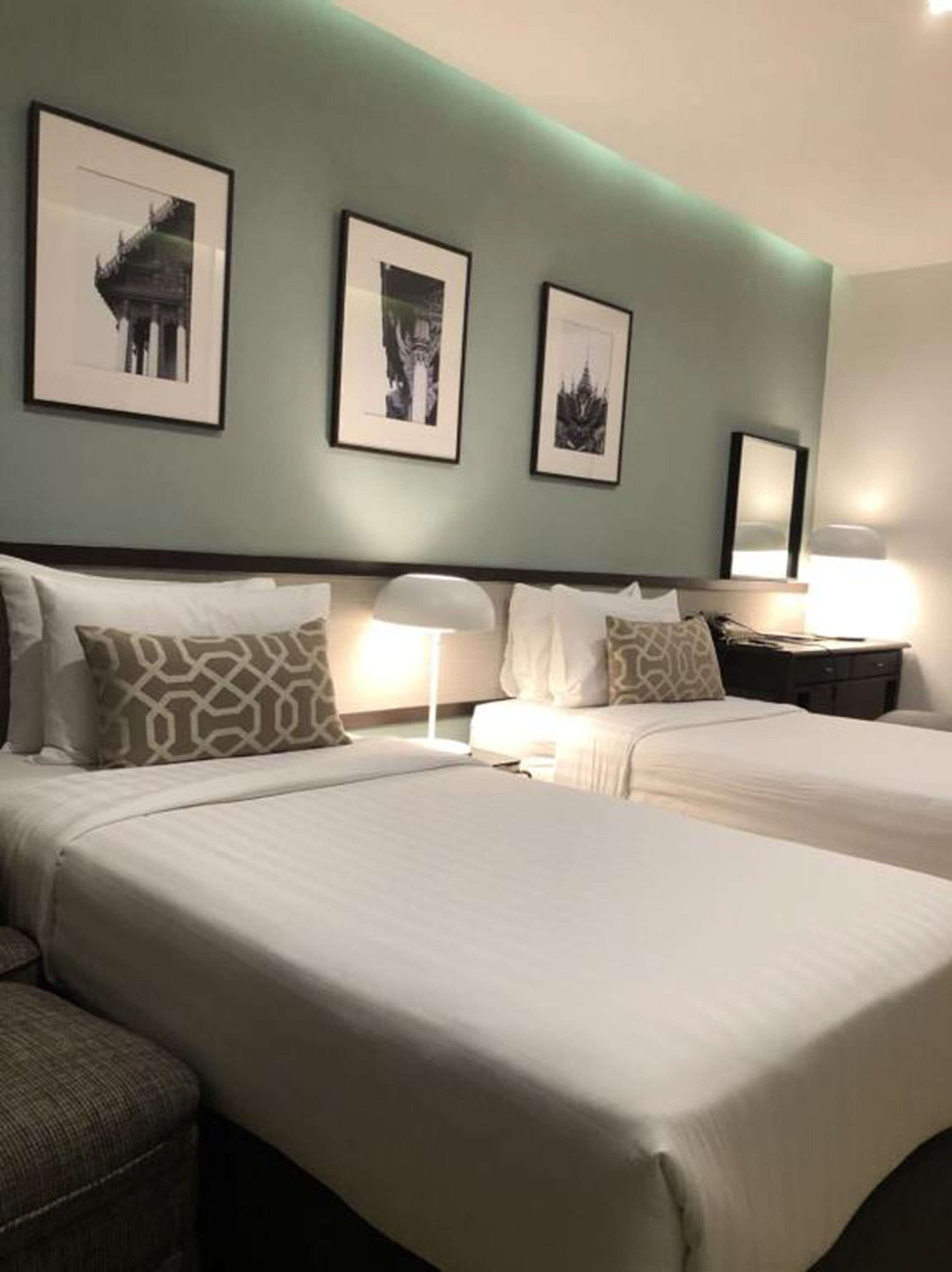 Habitación de hotel con dos camas, una mesita de noche con lámpara y tres cuadros enmarcados en la pared.