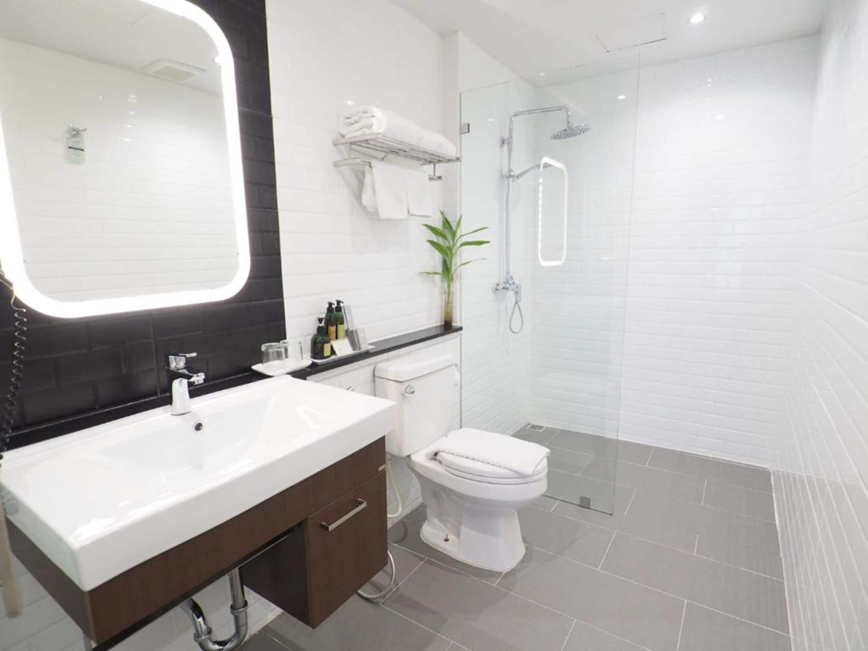A modern bathroom with a large mirror, white sink, and toilet.