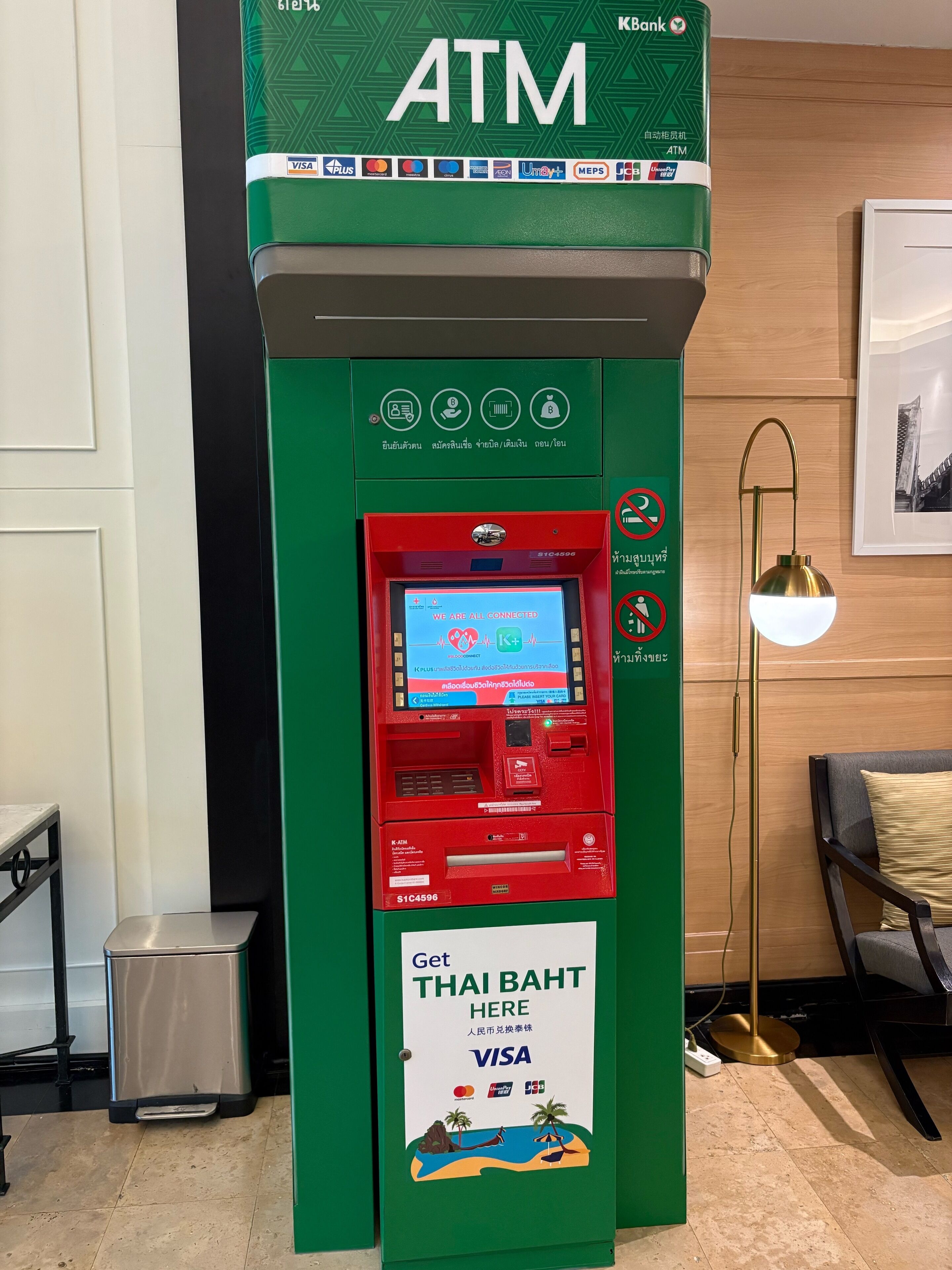 An ATM machine with a green and red color scheme, Visa and MasterCard logos, and a sign indicating Thai Baht currency.