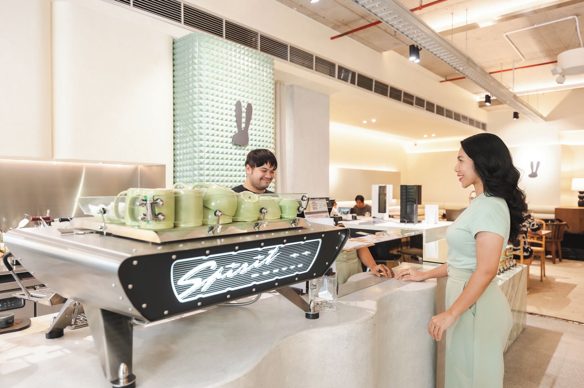 Una macchina da caffè dal design vintage, un bancone e una persona che vi sta dietro.