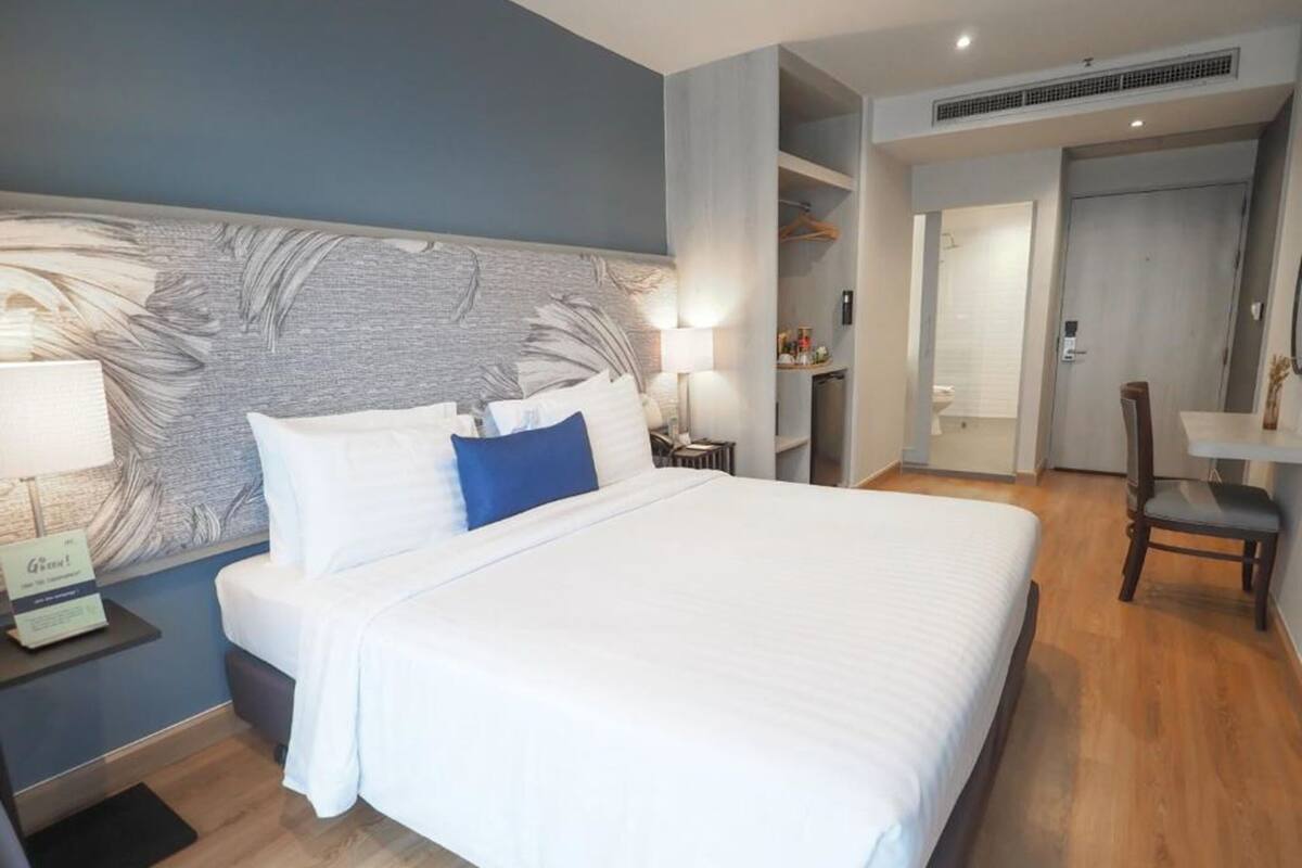 A hotel room with a large bed, a nightstand, a desk, and a chair.