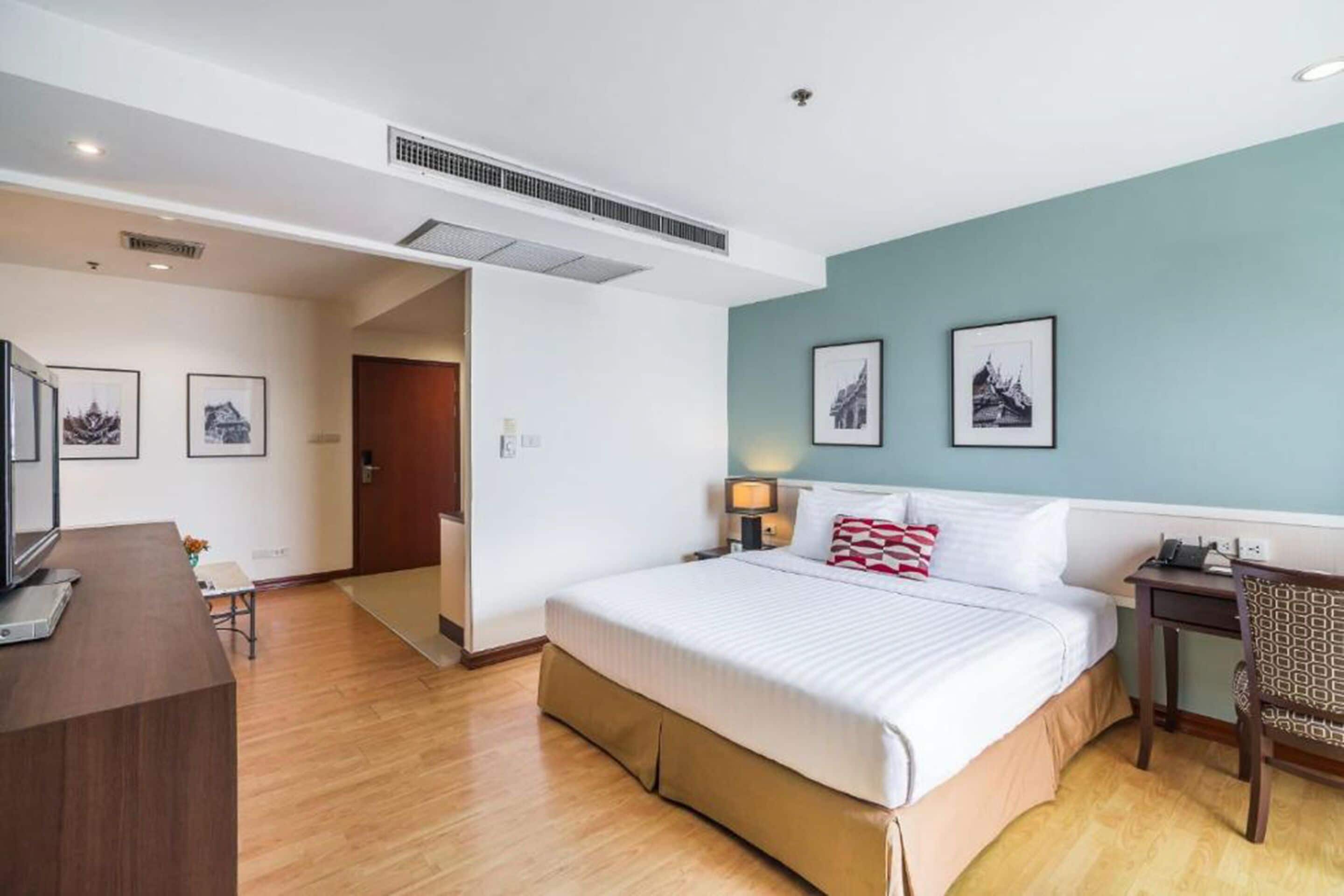 Una habitación de hotel con una cama grande, un escritorio, una silla y cuadros en la pared.