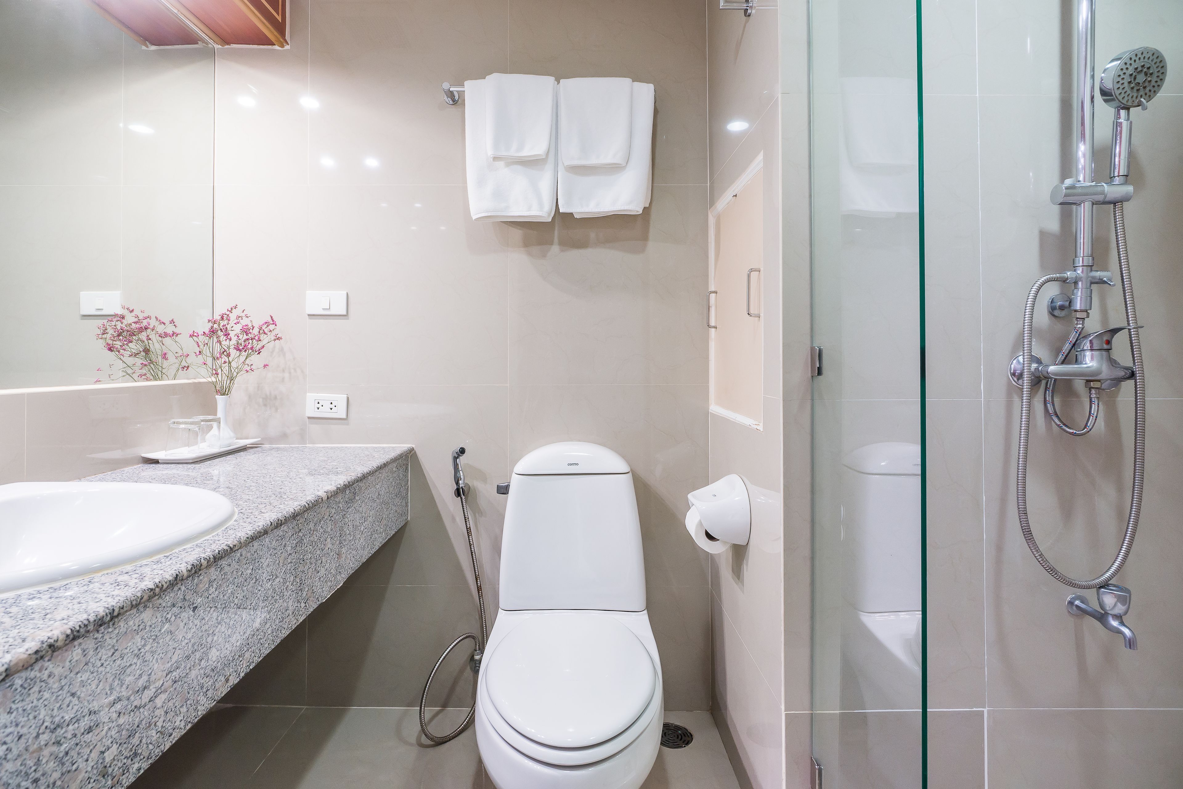 A modern bathroom with a granite countertop, a white toilet, a glass shower enclosure, and a towel rack with two towels.