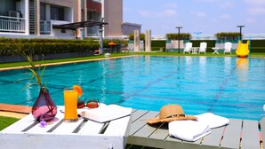 Un espace aménagé au bord de la piscine, avec des chaises longues, un vase contenant une plante, un verre de jus d’orange et une paille.