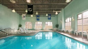 Una piscina interior con agua cristalina, rodeada de sillas de descanso blancas y una estructura de techo metálico.