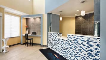 A reception area with a tiled counter, a chair, a vase with flowers, and a black reception mat.