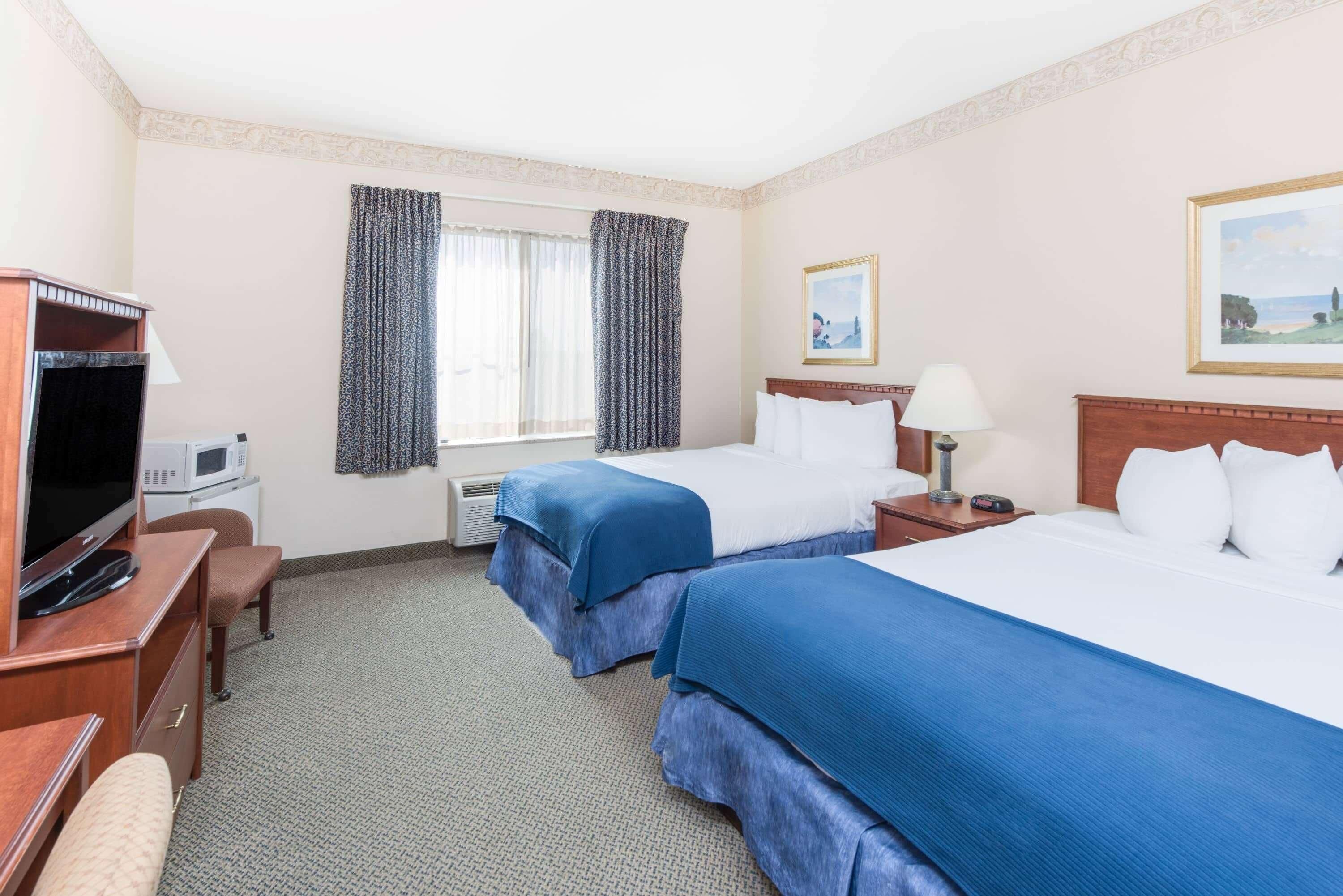 A hotel room with two beds, a TV, a desk, and a window with curtains.