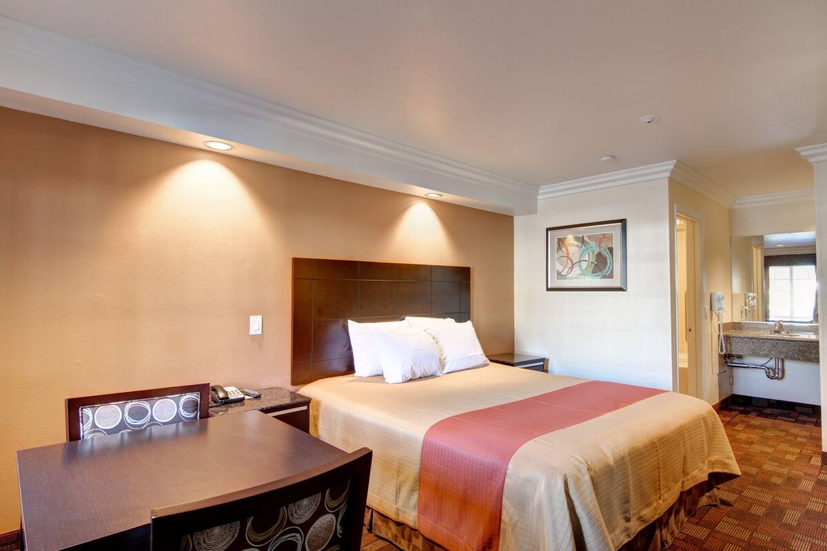 A hotel room with a bed, a desk, a telephone, and a bathroom with a sink and mirror.