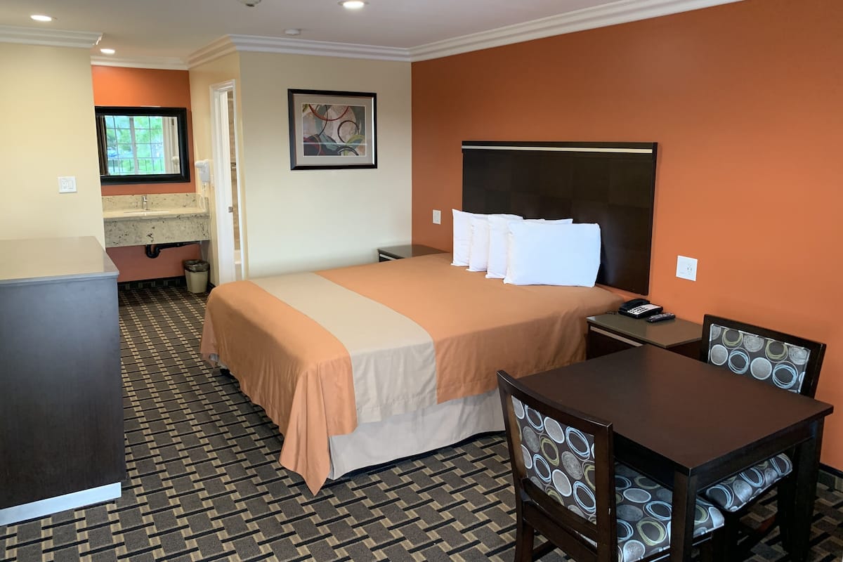 A hotel room with a bed, a desk, a chair, a sink, and a window.