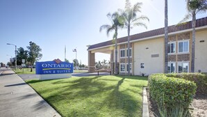 A sign for Ontario Inn & Suites with a well-maintained lawn and palm trees in front.