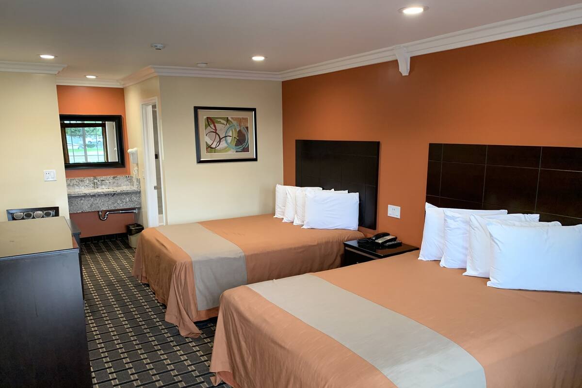 A hotel room with two beds, a small kitchenette, a bathroom, and a window.