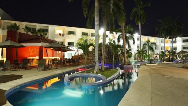 A pool area with a water feature, palm trees, and a building with a red sign. - La Isla Huatulco (Santa María Huatulco)