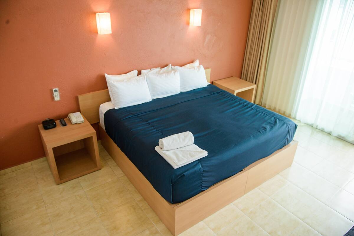 A hotel room with a large bed, two bedside tables, a wall-mounted phone, and a curtain.
