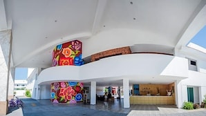A modern hotel lobby with a large, colorful floral mural on the wall, a reception desk, and a spacious open area.
