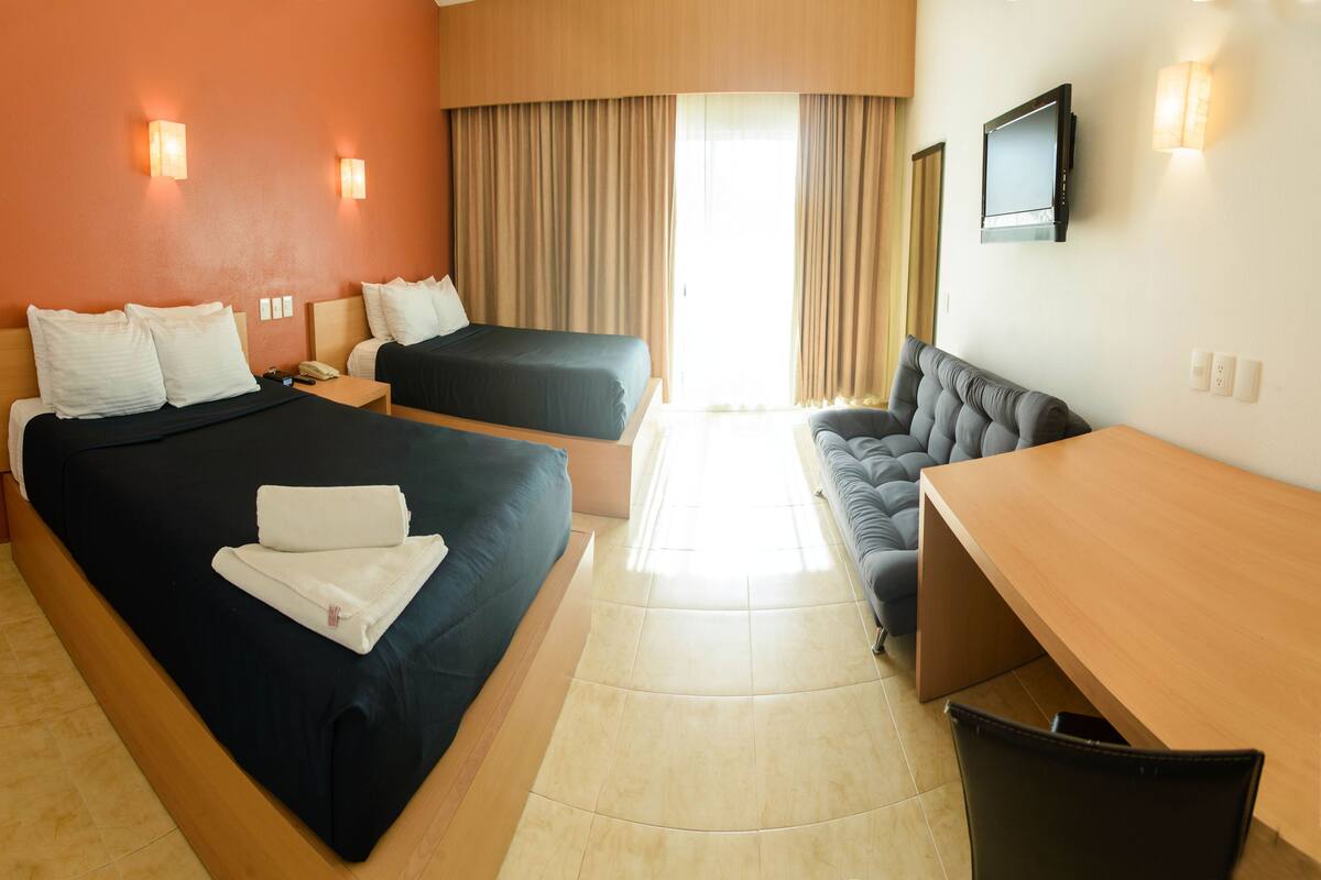 A hotel room with two beds, a sofa, a desk, and a TV.
