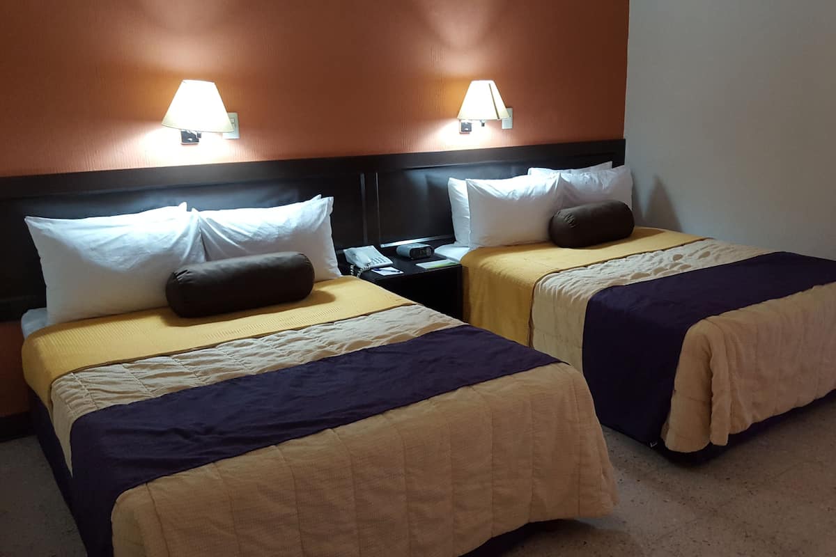 Two single beds with headboards, bedside tables, lamps, and a hanging coat rack.