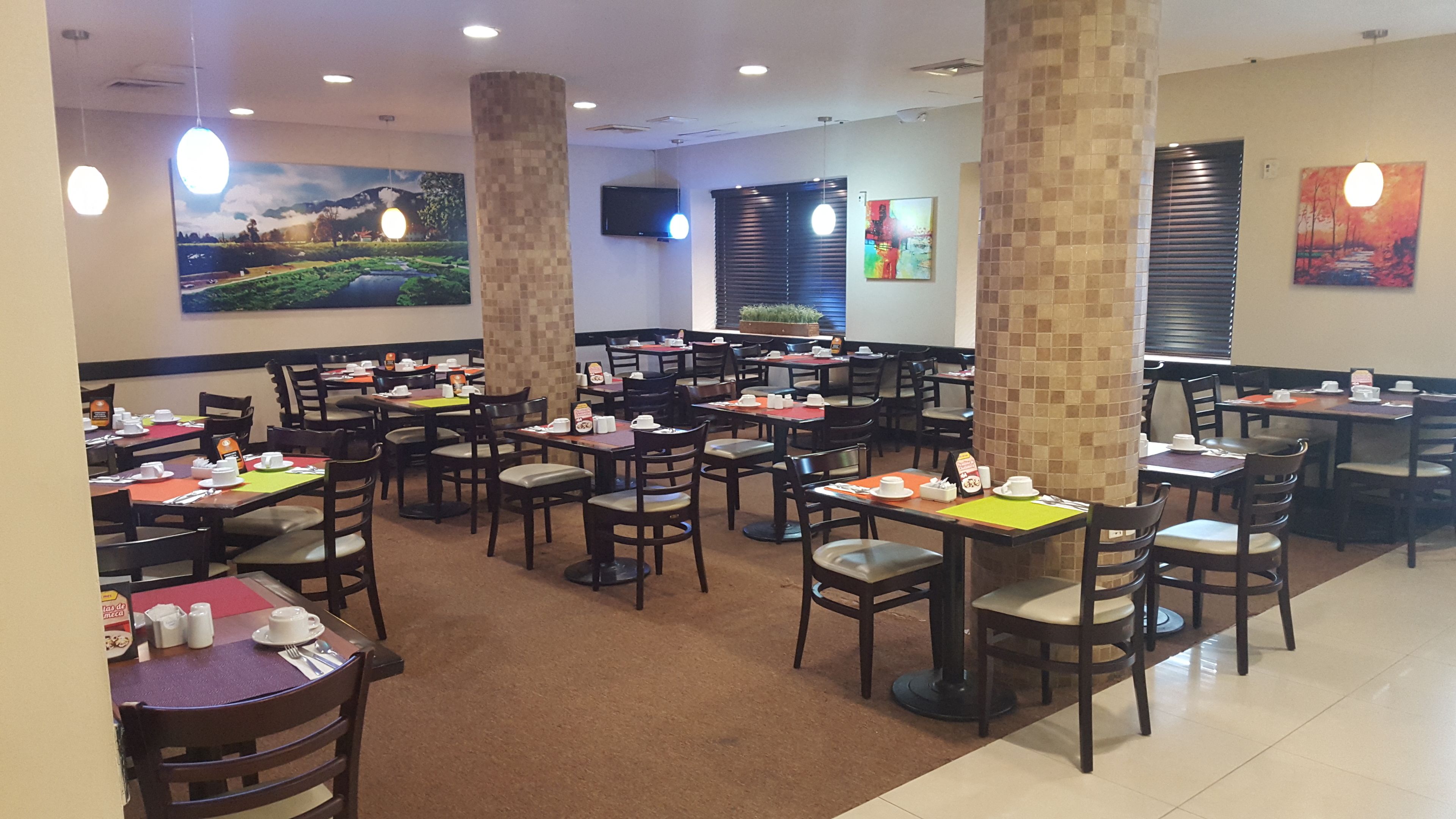 A restaurant with multiple tables and chairs, a tiled floor, and artwork on the walls.