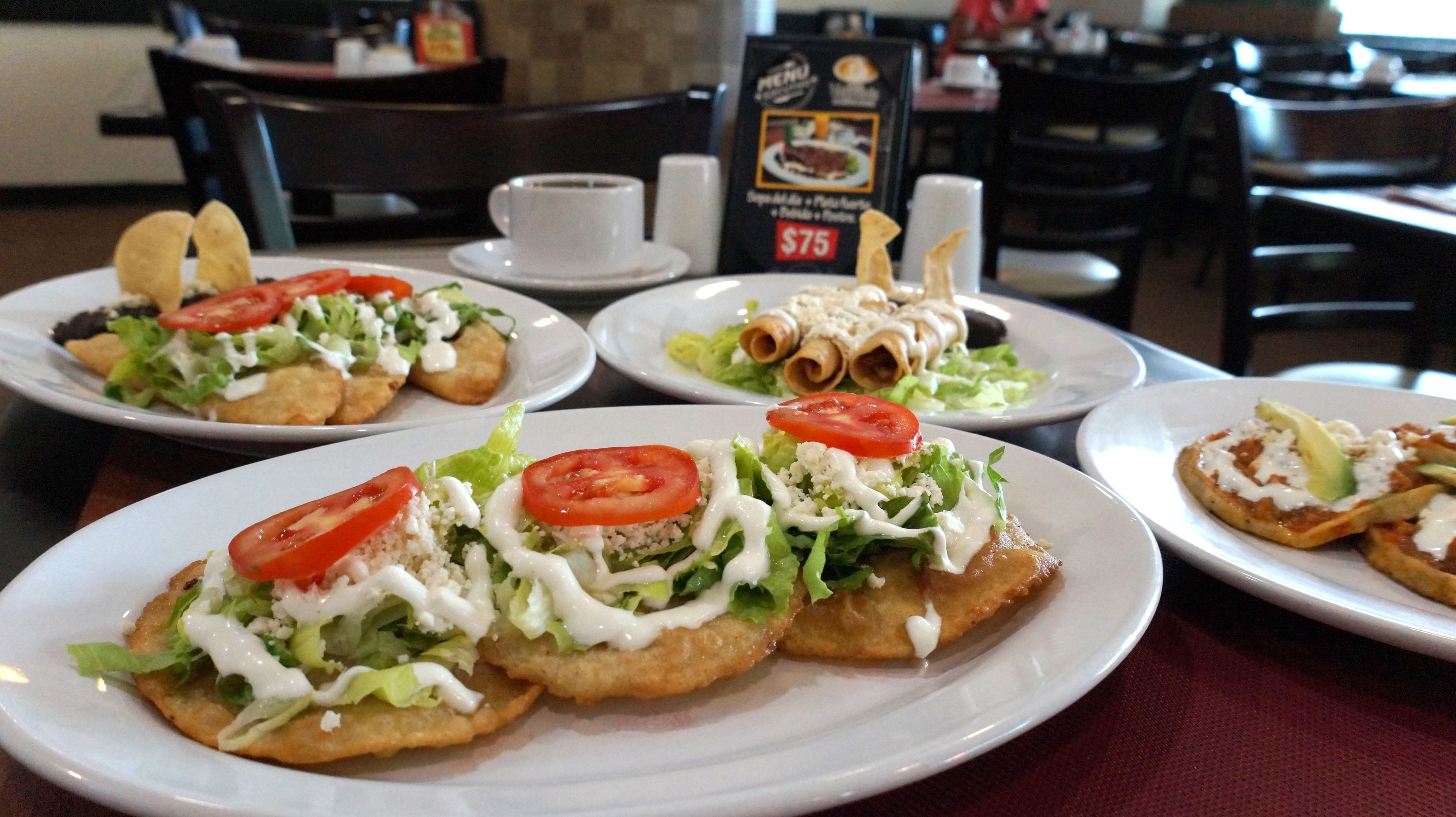 Um restaurante com mesas, cadeiras, pratos de comida e um letreiro com o cardápio.