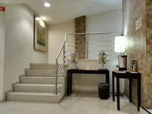 A staircase with a metal railing, a trash bin, a table with a coffee machine, and a wall-mounted sign. - Hotel Valgrande (Coatzacoalcos)