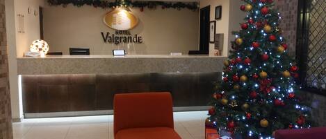 Zona de recepción de un hotel con un árbol de Navidad, un mostrador de recepción y una silla roja.