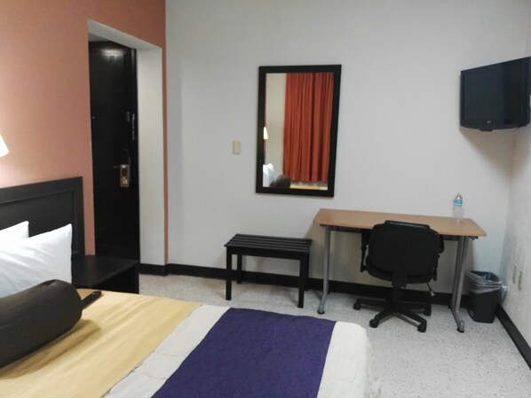 A hotel room with a bed, a desk, a chair, a trash bin, and a television on the wall. - Hotel Valgrande (Coatzacoalcos)