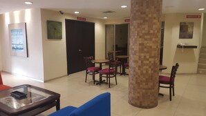 Um saguão de hotel com balcão de recepção, área de estar com mesas e cadeiras redondas e um grande pilar.