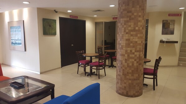 A hotel lobby with a reception desk, a seating area with round tables and chairs, and a large pillar. - Hotel Valgrande (Coatzacoalcos)