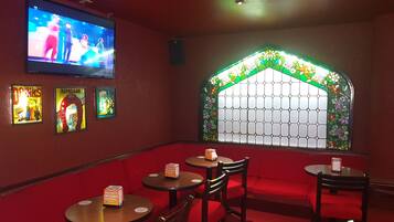 Ein Restaurantinneres mit Bildschirm, Buntglasfenster und Tischen mit Speisekarten.