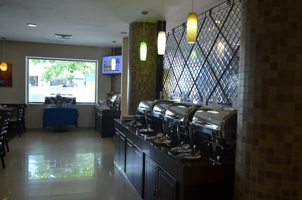 A buffet area with multiple self-service stations, a television screen, and a blue tablecloth-covered counter.