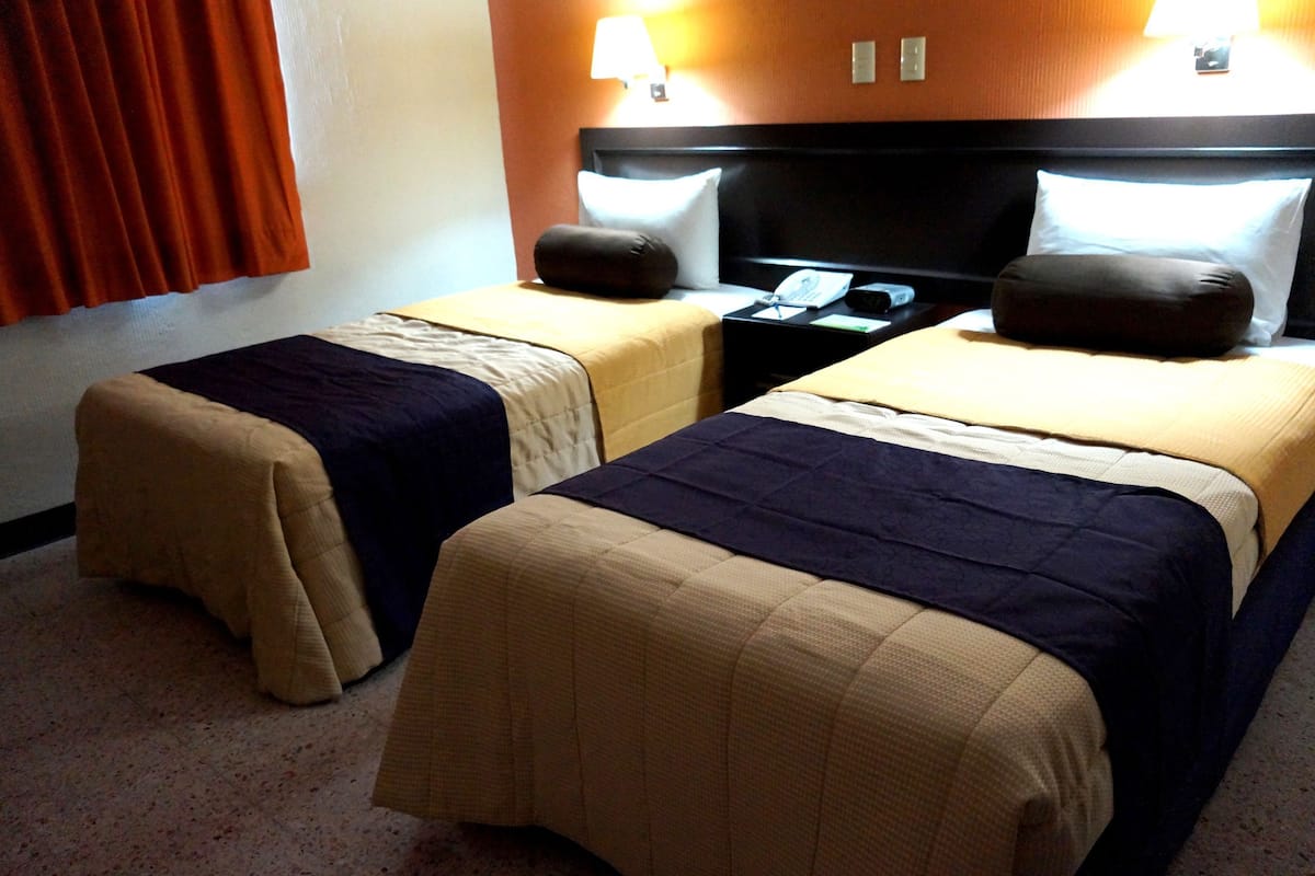 Two single beds with headboards, a nightstand with a lamp, and a window with curtains.