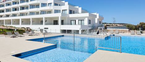 Un hotel moderno con piscina, varios balcones y una vista despejada de la costa.