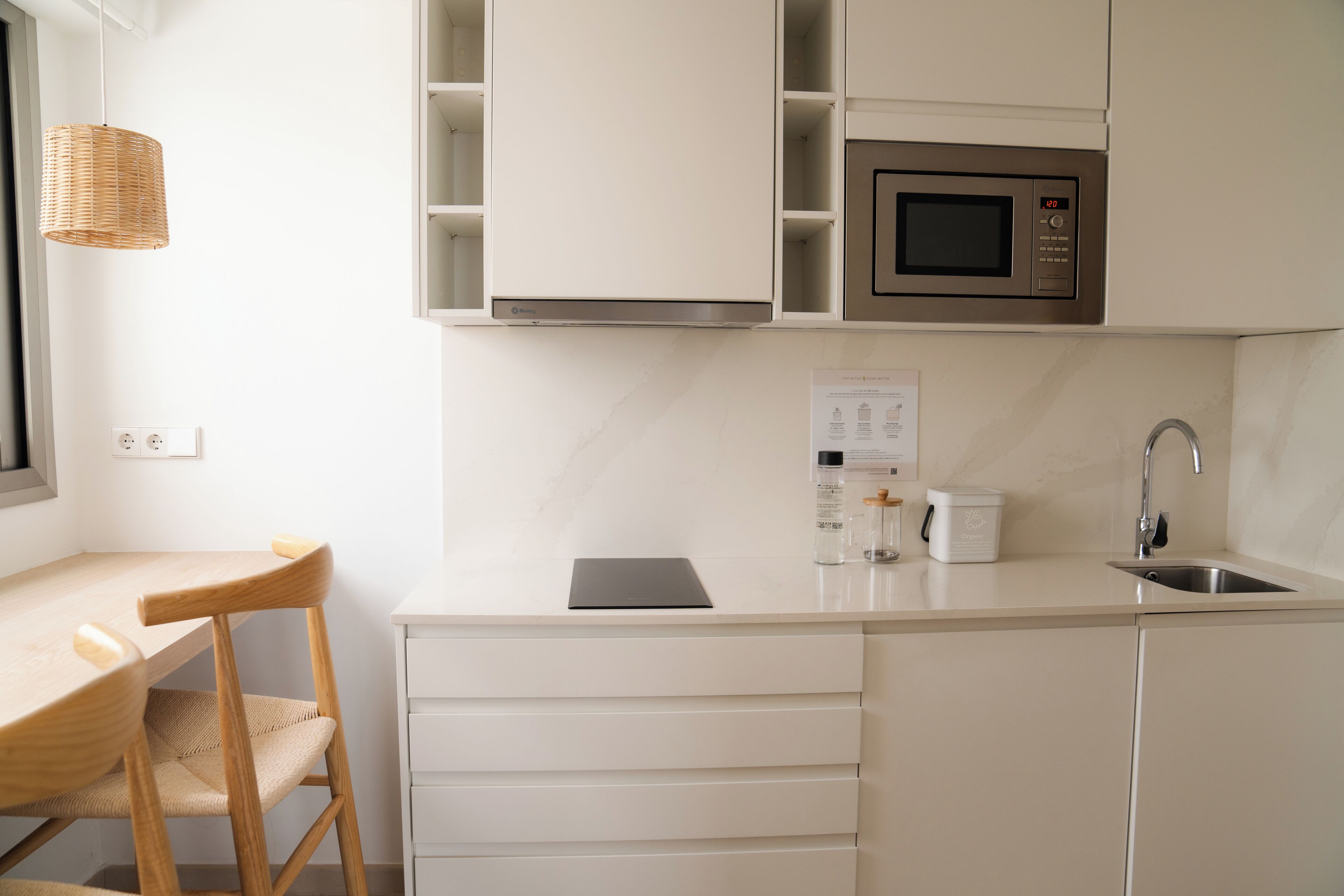 Eine moderne Küche mit weißen Schränken, einer Edelstahl-Mikrowelle, einem Spülbecken und einem Holzstuhl.
