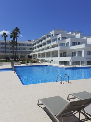 Un hotel moderno con piscina, palmeras y un cielo azul despejado.