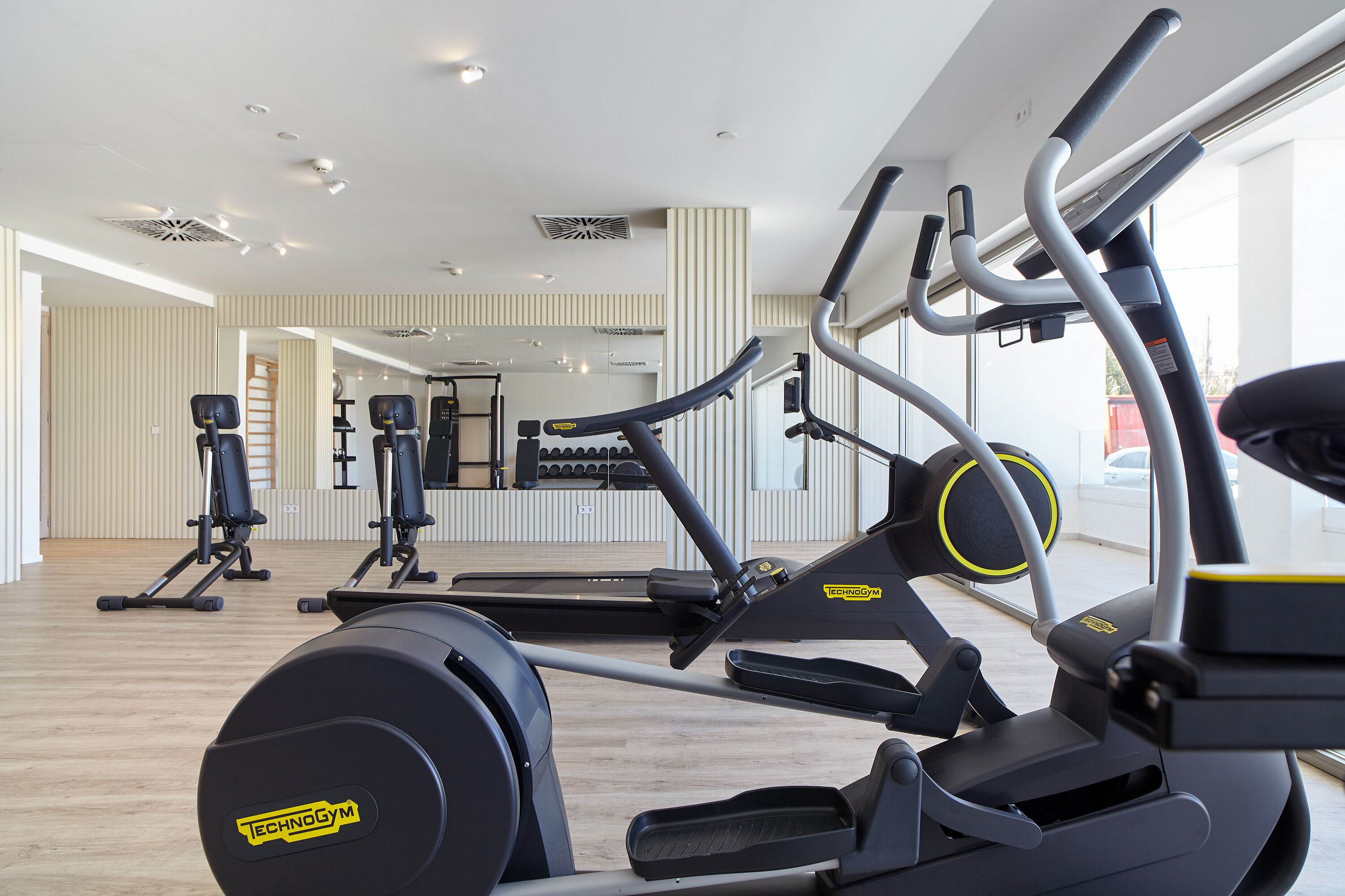 A gym with cardio machines, mirrors, and a wooden floor.
