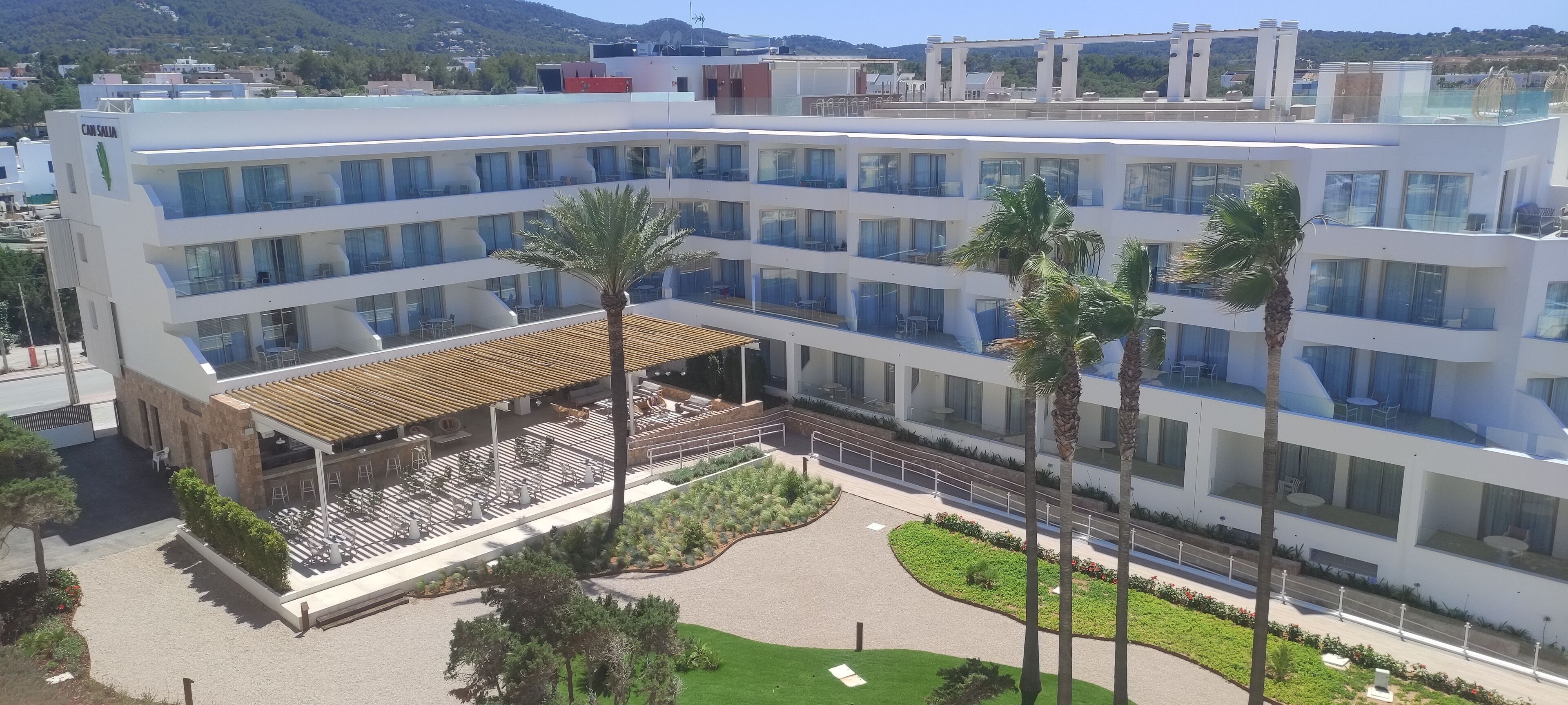 Un hôtel à plusieurs étages doté de balcons, d’un espace extérieur couvert avec des sièges et de palmiers.