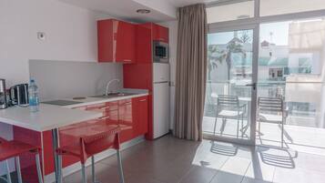 Une cuisine moderne avec des meubles rouges, un plan de travail blanc et une porte vitrée donnant sur un balcon équipé de chaises.
