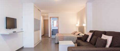 A modern living room with a sofa, a TV mounted on the wall, and a hallway leading to a bedroom.