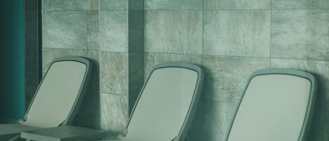 Three white lounge chairs aligned against a tiled wall in a public area.