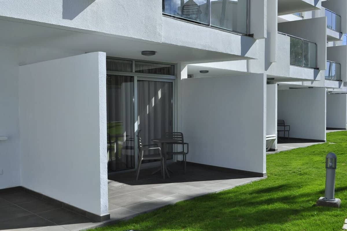 A modern building with a flat roof, large windows, and a small patio area with chairs and a table.
