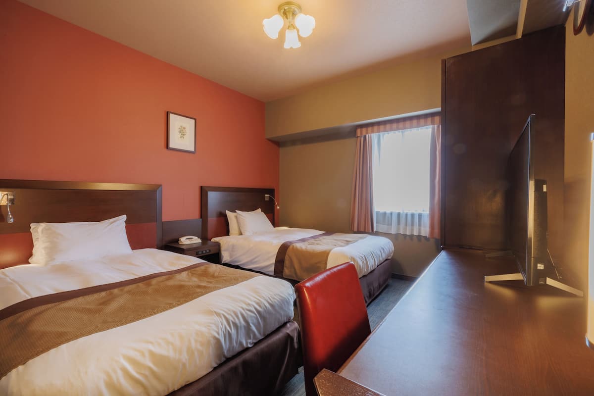 A hotel room with two beds, a desk, and a chair.