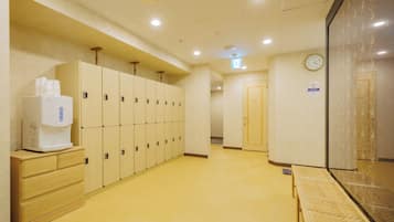 A hotel corridor with lockers, a coffee machine, a clock, and a seating area.