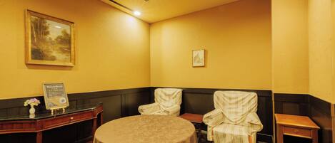 A room with a round table, two chairs, a small table, a cabinet, and a wall-mounted picture.