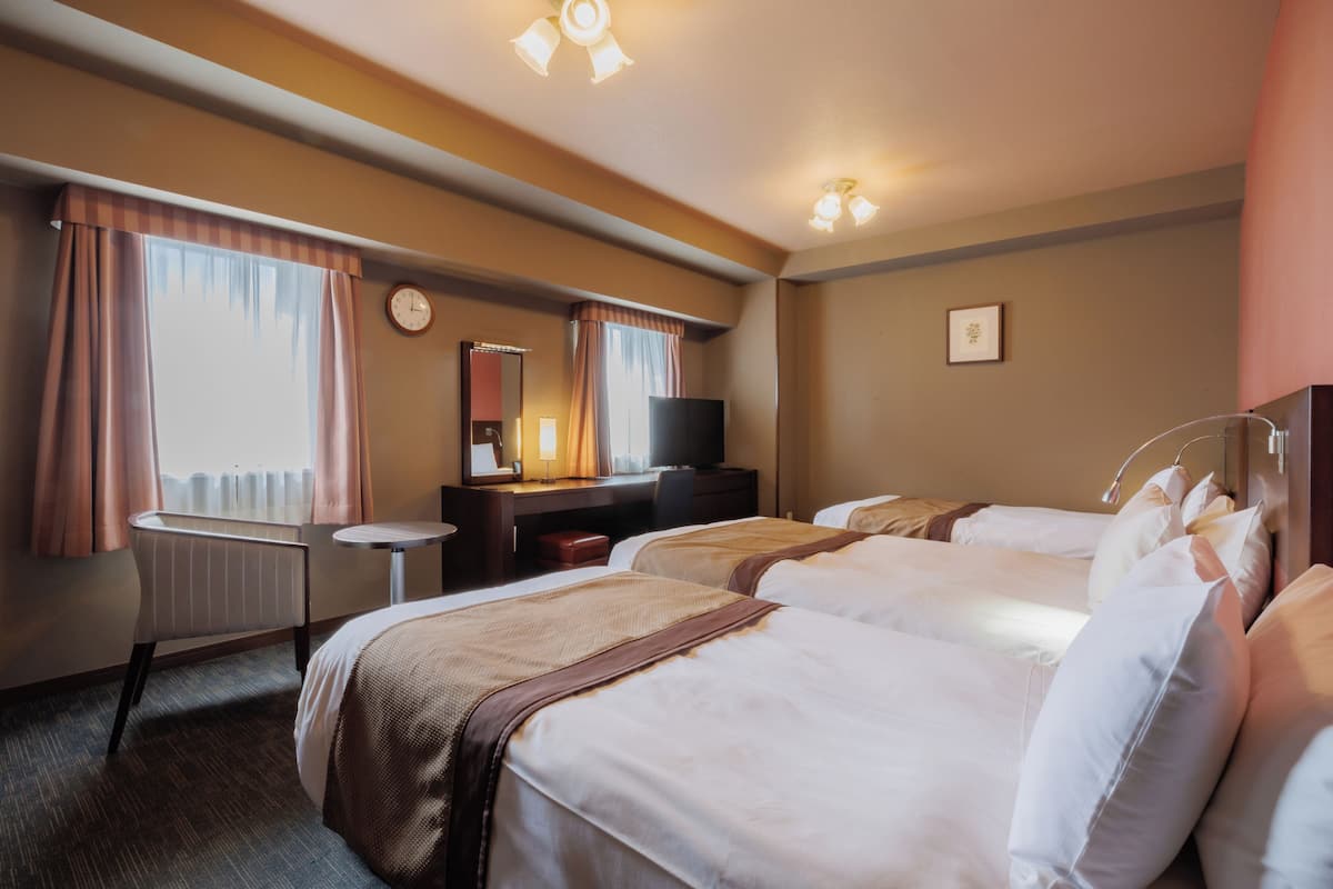 A hotel room with two beds, a desk, a chair, a television, and a clock on the wall.