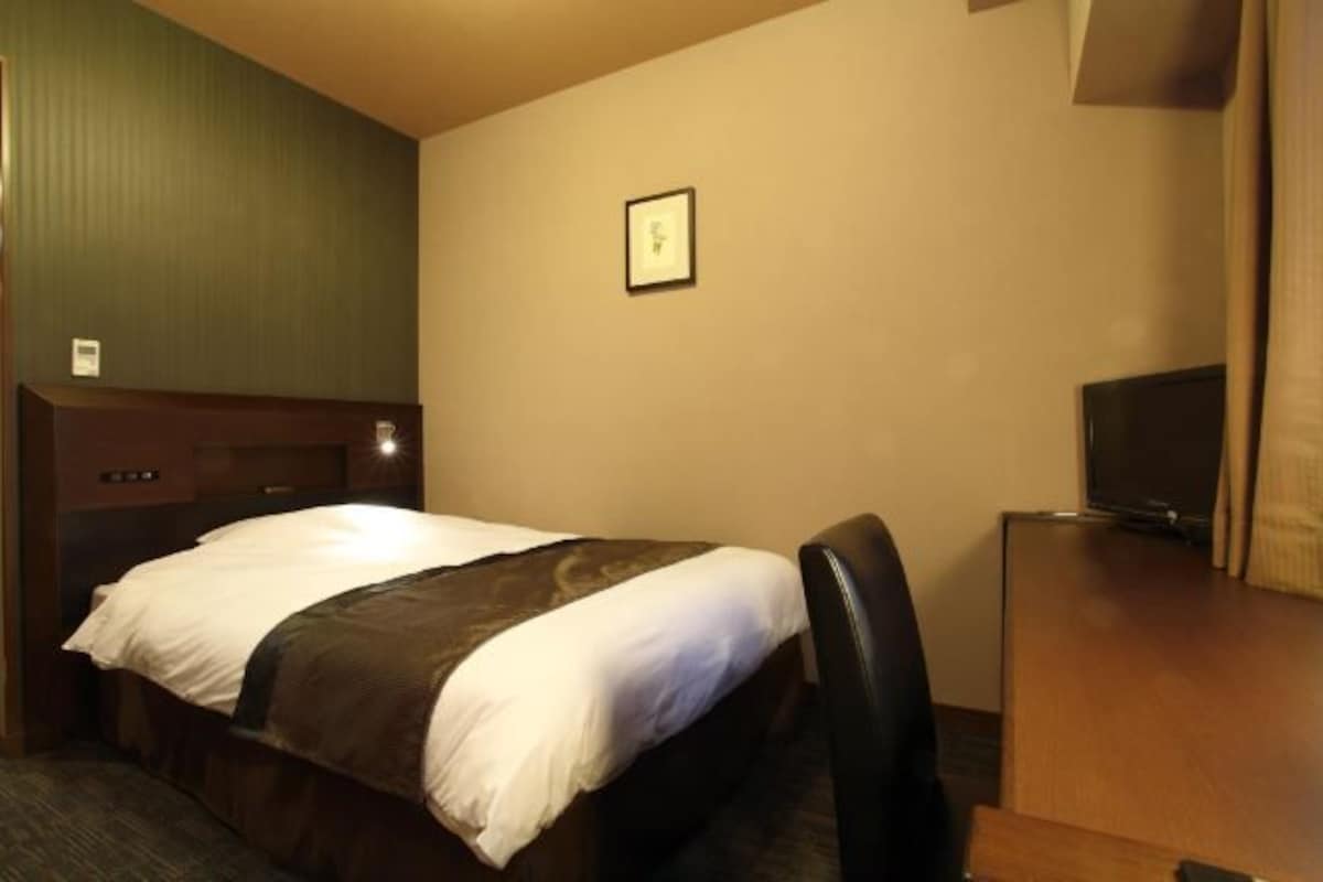A hotel room with a bed, a desk, a chair, a television, and a framed picture on the wall.